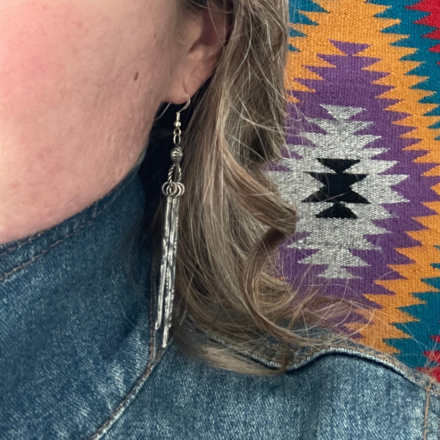 A woman wearing Sterling Silver dangle earrings on French hooks featuring hand stamped design standing in front of a genuine Navajo rug