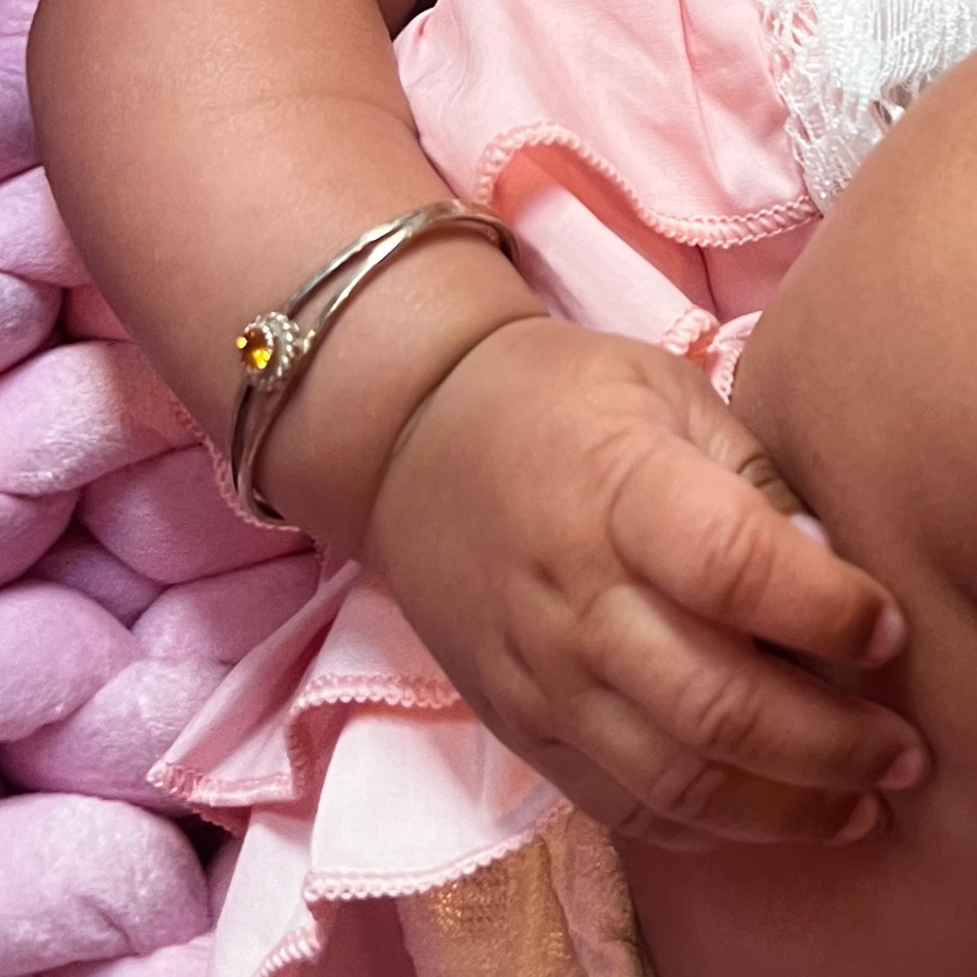 Close up of baby's arm resting on her chubby leg, on her wrist is a handmade Sterling Silver baby bracelet by Caleb Calles with her birthstone, Citrine, November