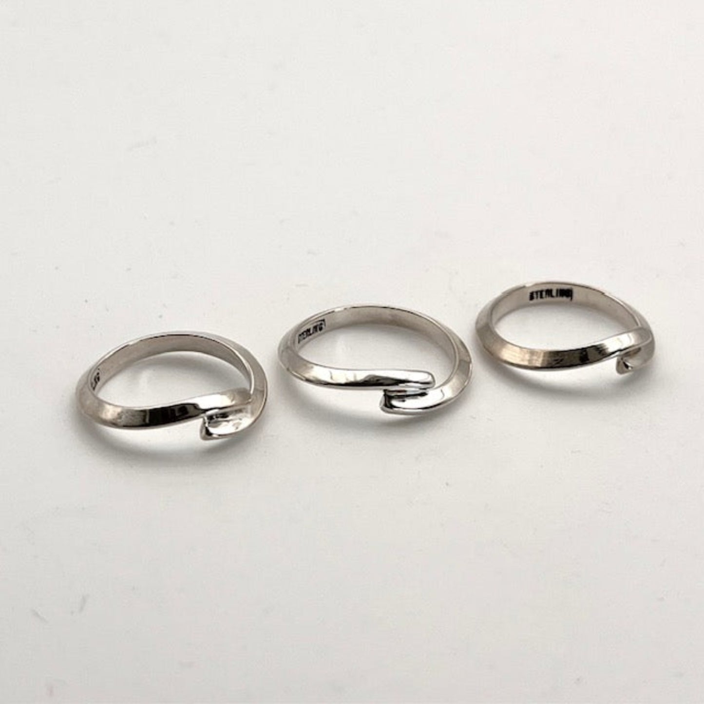 Three silver handmade rings on a white background stamped Sterling