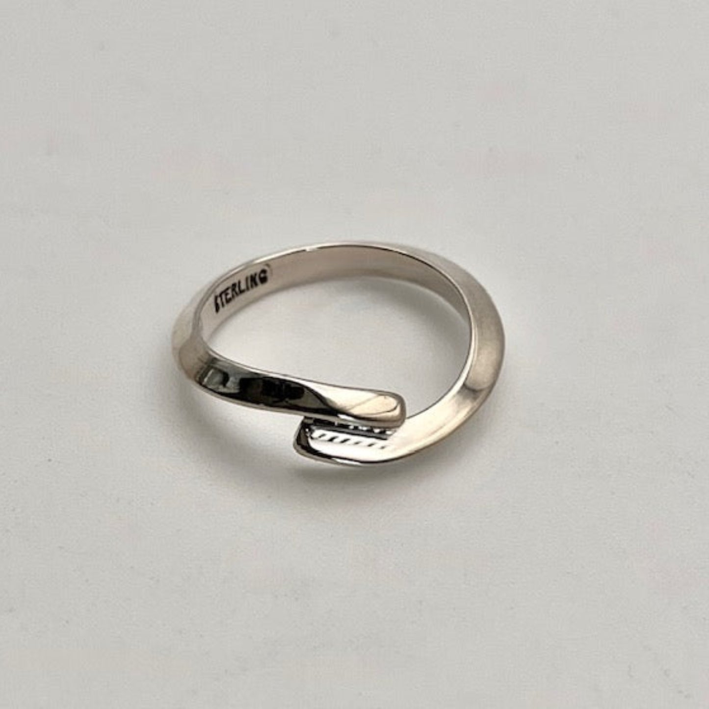 Silver ring with 'STERLING' engraving on a light gray background