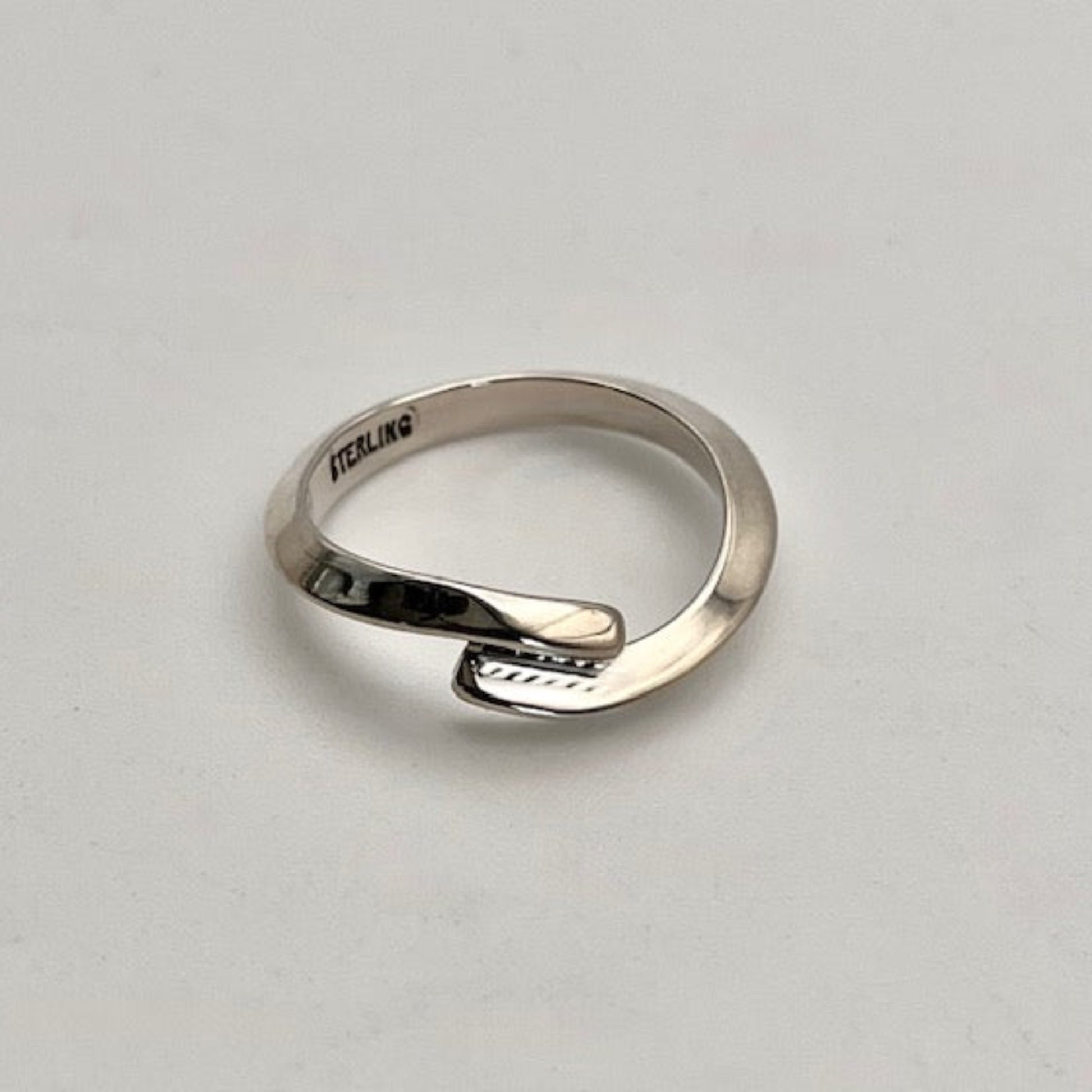 Silver ring with 'STERLING' engraving on a light gray background